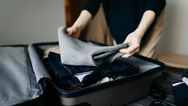 Woman packing a suitcase on bed for a trip at home 