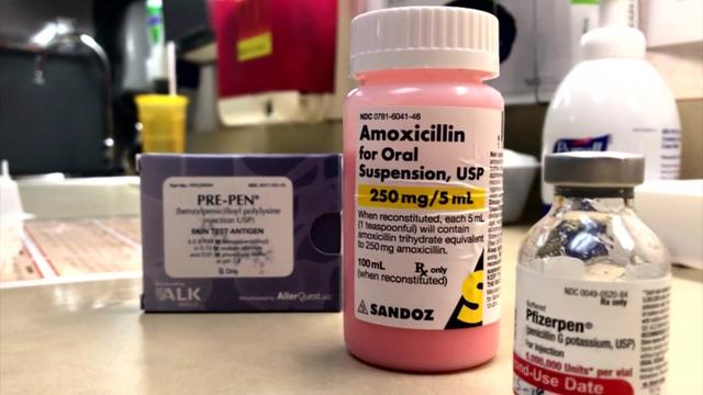 A bottle of amoxicillin sits on a desk with a bottle of penicillin and a pre-pen 