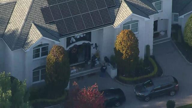 An aerial shot of law enforcement agencies outside a large house in Holmdel. Several boxes sit on the front stoop. 