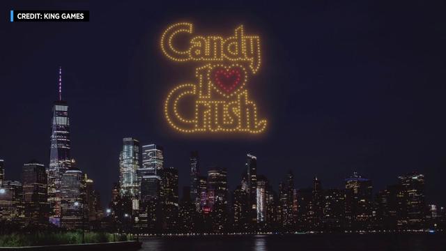 An artist's rendering shows the words "Candy 10 Crush" spelled out with lighted drones over a nighttime skyline. 