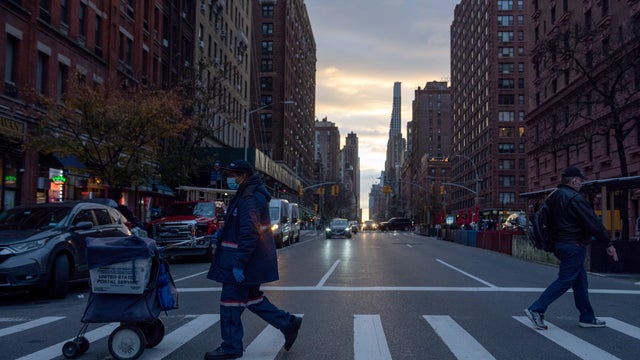 A USPS worker wearing a mask crosses the road during sunset on December 05, 2020 in New York City. 