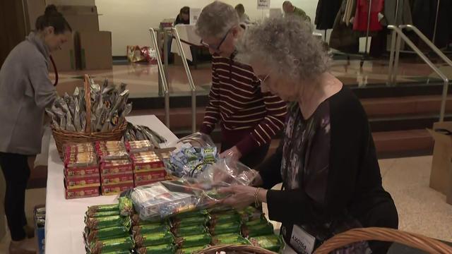 Volunteers stand at a table packing bags with food. 