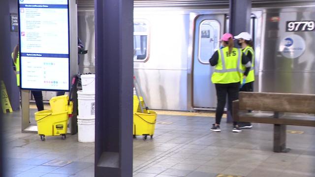 Subway custodians stand on a train platform. 