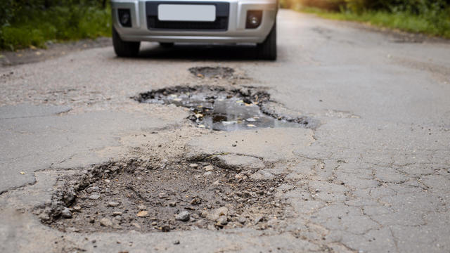 Road in terrible condition. Photo of a road with many potholes, chuckholes and driver driving the car very slow in order not to damage his vehicle 