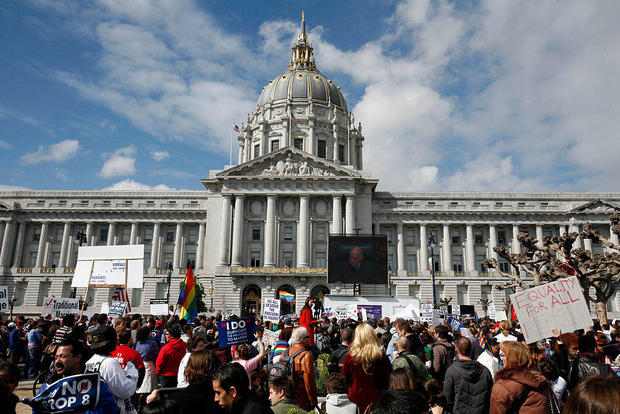 SANFRANCISCO,CA: People gather to watch a large television screen at City Hall prior to the Califor 
