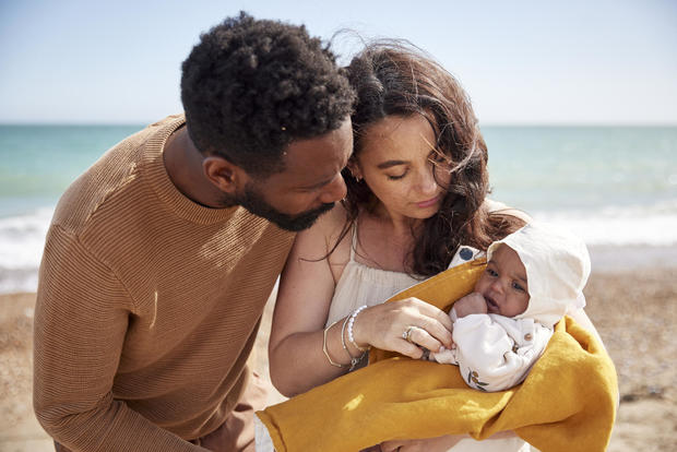 Mother and father, adoringly looking at their newborn daughter, on the beach enjoying their first trip to the shore. 