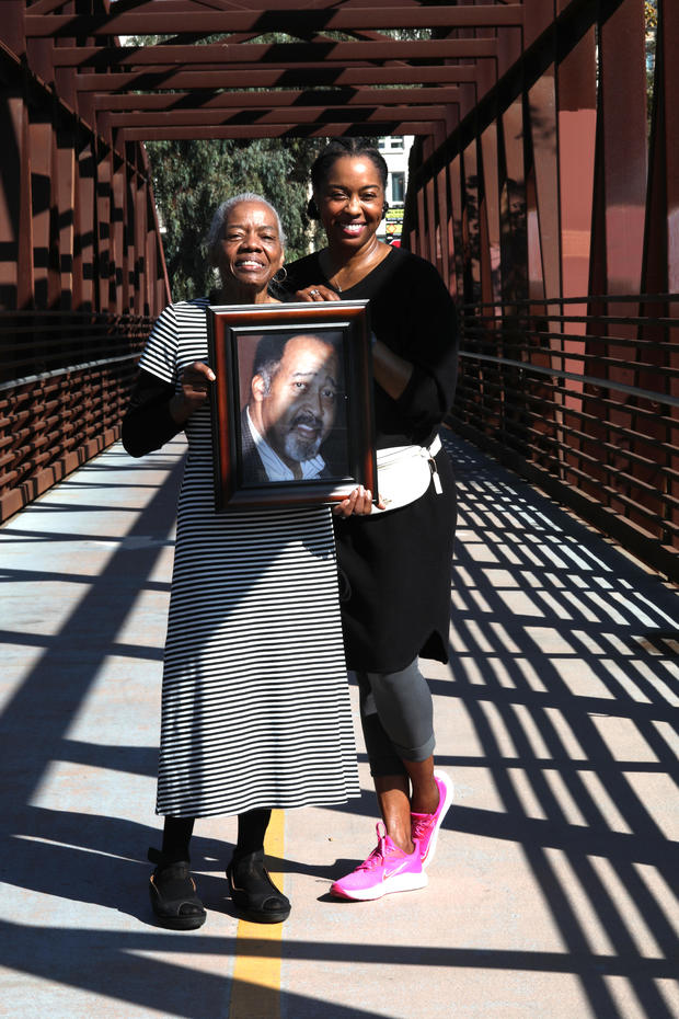 Catherine Lawson (left) carrying a picture of her husband Jerry Lawson with her daughter Karen Lawson (right) seen on a bridge over the Guadalupe River on Thursday, Nov. 5, 2020, in San Jose, Calif. 