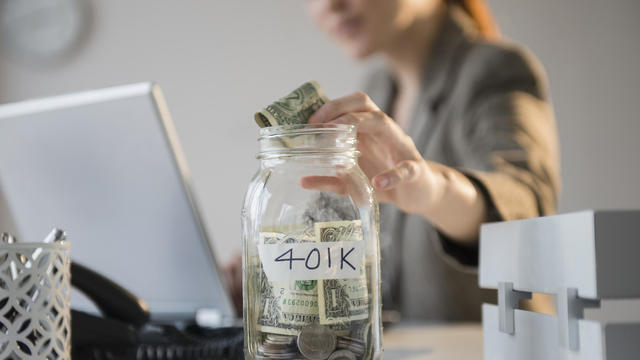 Businesswoman putting money into 401K jar at desk 