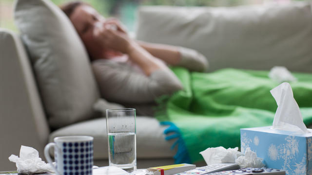 Sick woman laying on sofa blowing nose 