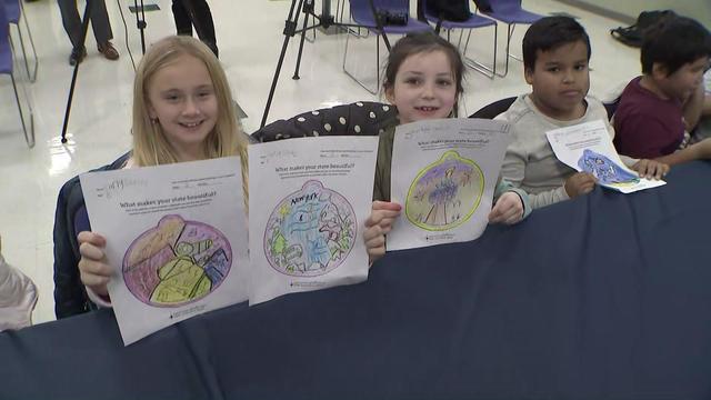 Students hold up drawings of ornaments they designed showing what makes New York beautiful. 