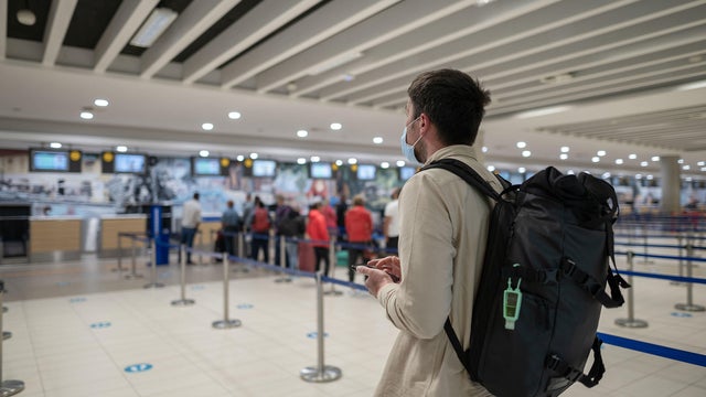 Man in protective mask with phone at airport departure check-in desk for baggage drop-off at terminal and check-in for flight, maintains social distance. Travel during covid 19 pandemic. New normal 