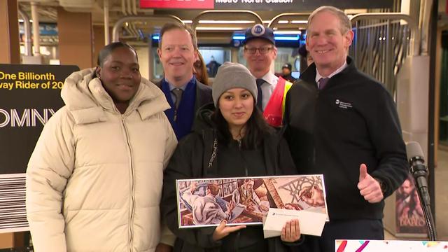 Sasha Salazar poses with MTA officials in a subway station, holding a framed piece of subway art. 