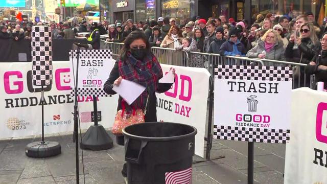 A woman tears up a piece of paper and puts it in a trash can at Good Riddance Day in Times Square. 