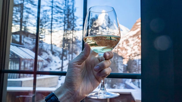 Man Holding Wineglass Against Matterhorn Seen Through Glass Window At Resort