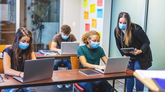 High School Students and Teacher wearing face masks and social distancing in Classroom Setting working on laptop technology 