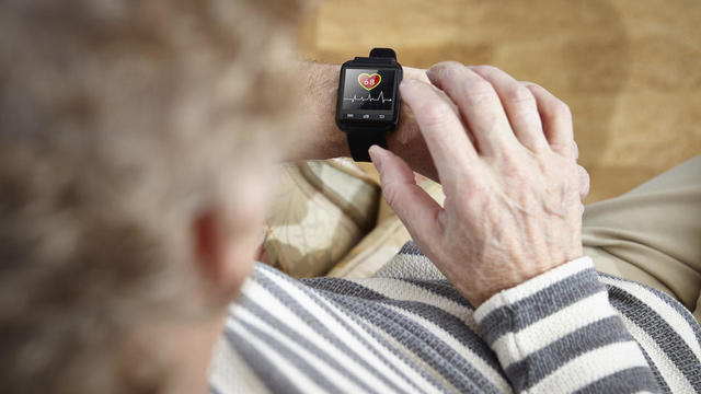 Senior man sitting in armchair using smartwatch 