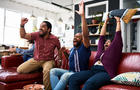 Friends watching TV at home and cheering with arms raised 