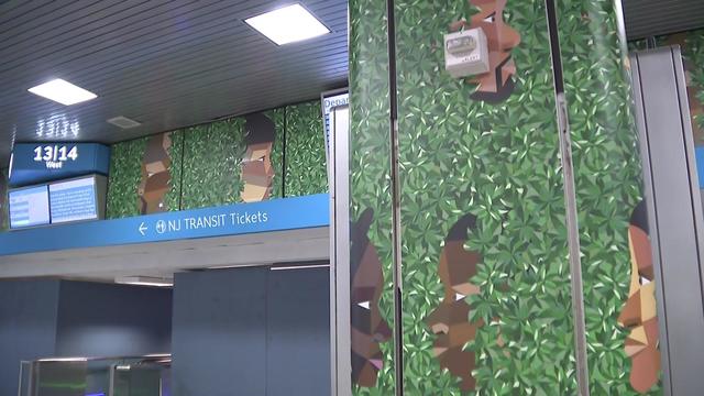Artwork on display in Penn Station shows faces peering out of greenery. 