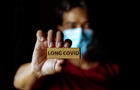 Masked Asian man show wooden sign with wording "Long Covid" 