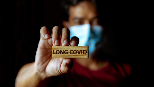 Masked Asian man show wooden sign with wording "Long Covid" 