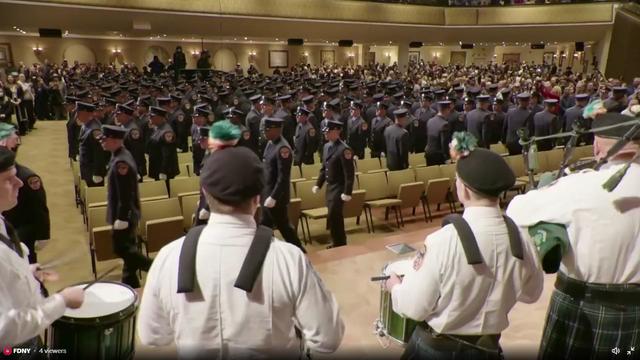 Dozens of file into an auditorium in front of drummers and bagpipers. 