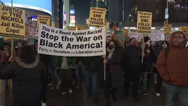 A crowd of protesters carrying signs walks down the street in Times Square. 