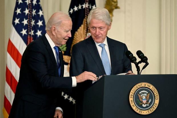 President Biden helps former President Bill Clinton find his notes during an event marking the 30th anniversary of the Family and Medical Leave Act in the East Room of the White House on Feb. 2, 2023. 