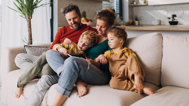 Little children bonding with parents on sofa at home and using tablet. 