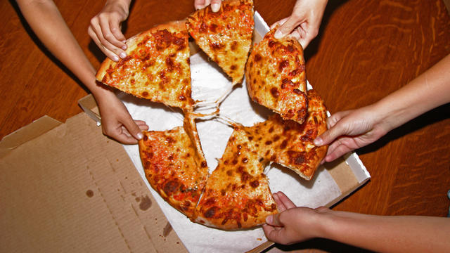 People grabbing slices of pizza, overhead view 