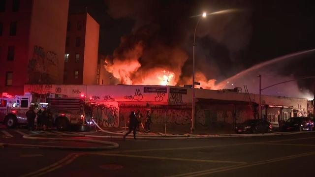 Flame can be seen shooting from the roof of a Bronx supermarket at firefighters spray it with water. 