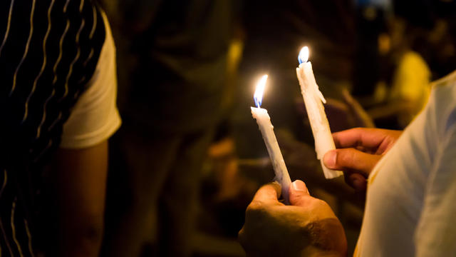 People holding candle vigil in darkness 