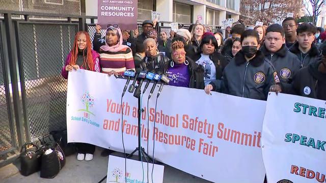 Dozens of people stand behind a sign reading "Youth and School Safety Summit and Family Resource Fair." 