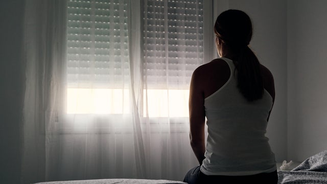 Rear view of an unrecognizable abused woman sitting on her bed looking out the window.
