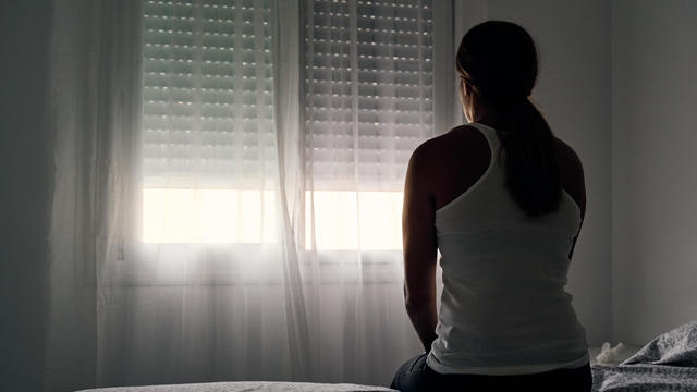 Rear view of an unrecognizable abused woman sitting on her bed looking out the window. 
