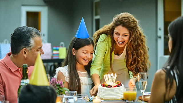 Smiling woman holding cake by birthday girl 