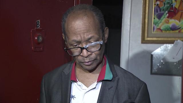 Pierre Augustin stands outside his apartment. His broken glasses have been repaired with Scotch tape. 