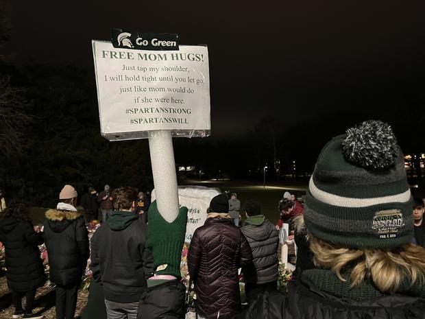 Woman holding sign that says, "Free mom hugs! Just tap me on the shoulder, I will hold tight until you let go, just like mom would do if she were here. #SpartanStrong #SpartansWill 