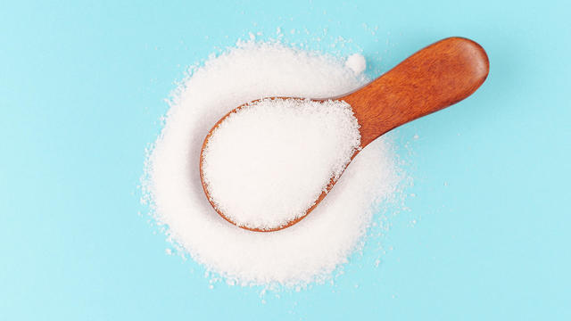 Erythritol powder in a wooden spoon close-up on blue background. 