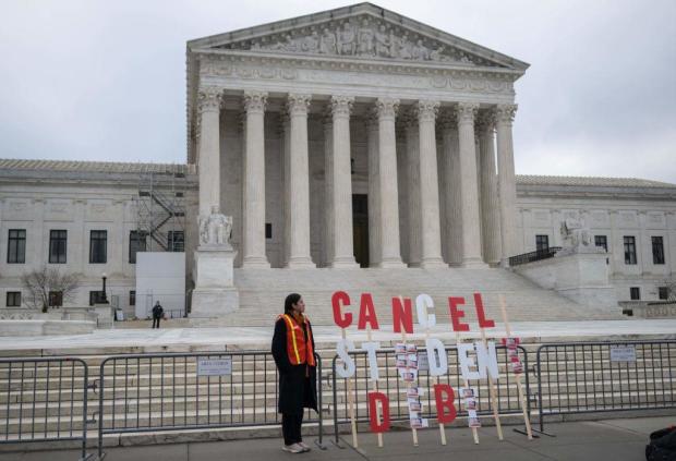 An activist stands next to a sign as they protest in front of the Supreme Court during a rally for student debt cancellation on Feb. 28, 2023. 