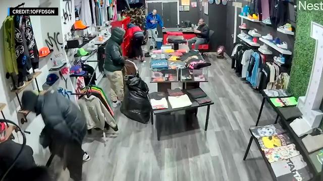 Surveillance video shows several people filling garbage bags with merchandise inside a clothing store. 