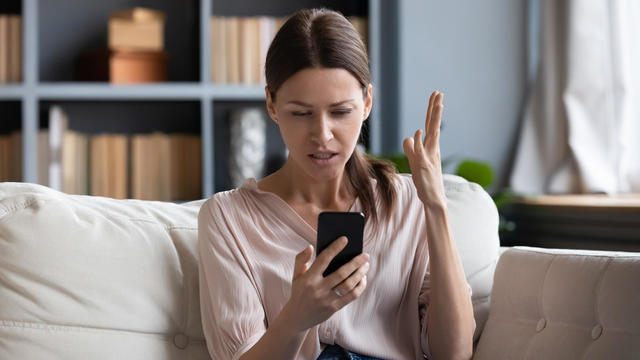 Confused angry young woman having problem with phone 