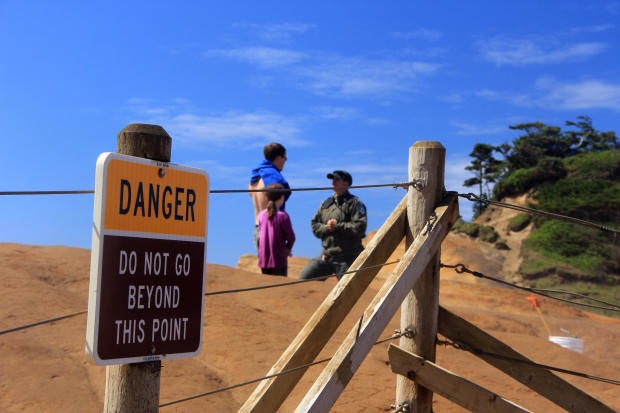 A park ranger with the Oregon Parks and Recreation Department talks to a man and his daughter who walked through the fence at Cape Kiwanda State Natural Area in Cloverdale, Oregon, June 29, 2016. 
