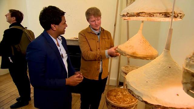 Two individuals look at lampshades made using mycelium. 