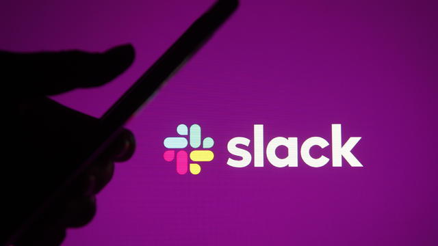 Someone holding a phone against the backdrop of the Slack logo 