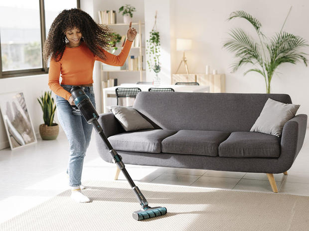 Smiling young woman with vacuum cleaner dancing in living room at home 