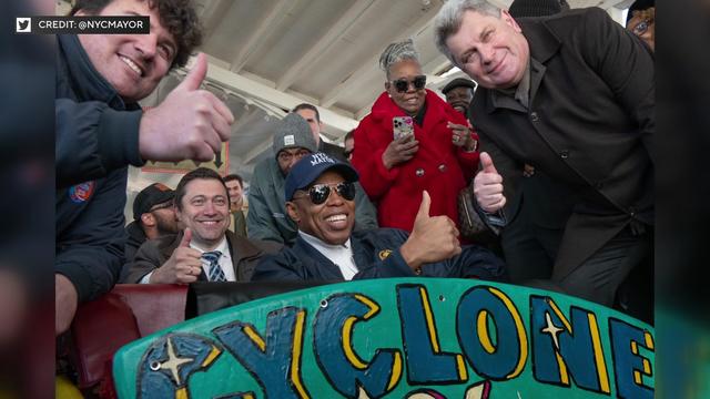 Mayor Eric Adams and a number of other individuals give a thumbs up to the camera while posing on the Cyclone. 