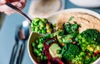Eating vegan bowl with edamame beans, broccoli, avocado, beetroot, hummus and nuts 