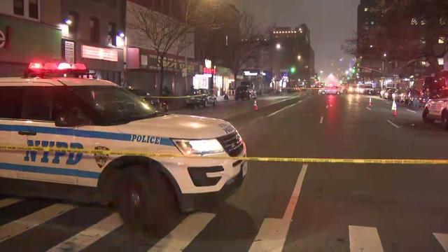 A street is blocked off by crime scene tape and police vehicles. 