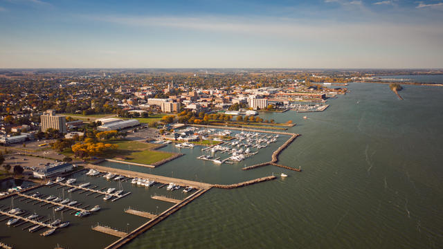 Incredible aerial city skyline panorama photograph of Sandusky, Ohio from the shoreline of the bay in Lake Erie with parks and harbors seen below on a sunny day. 