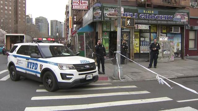 An NYPD vehicle is parked on a street corner outside a deli blocked off by crime scene tape. 